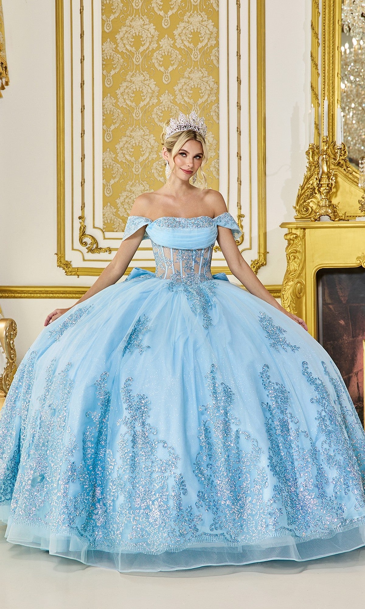 A woman wearing the Quinceanera Dress 5123 By Dancing Queen in Bahama Blue with a tiara stands in an ornate, gold-accented room.